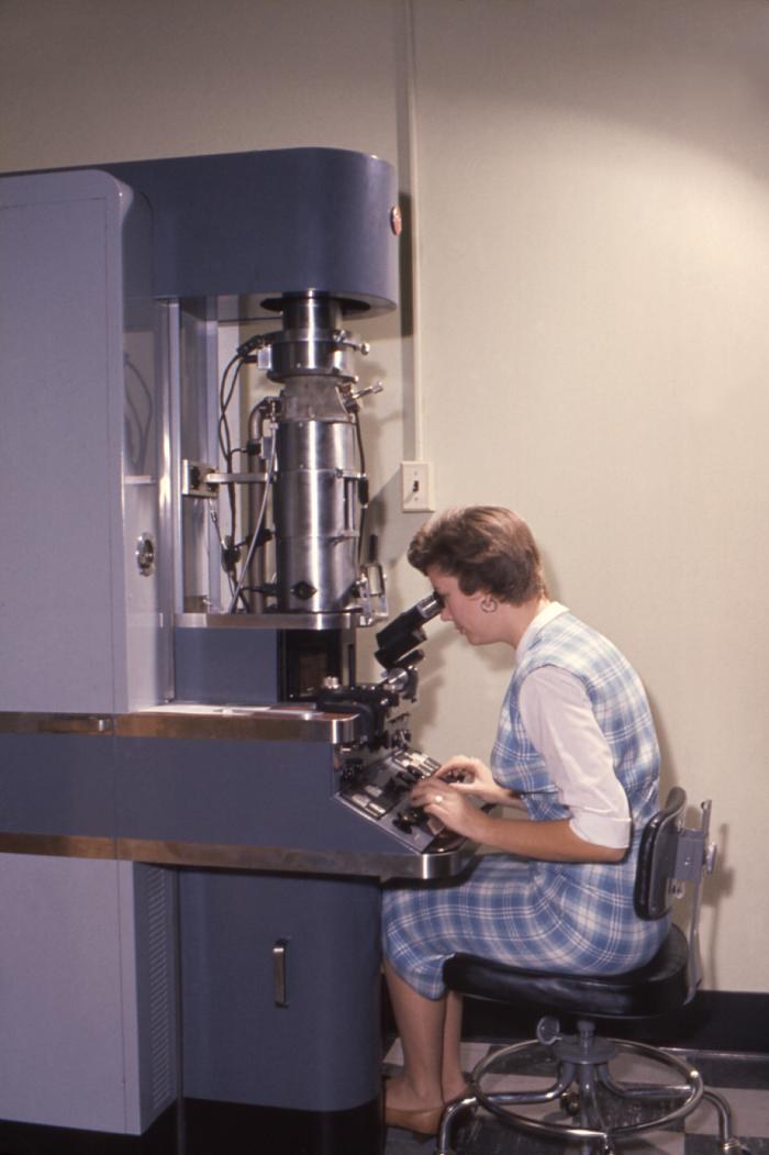 1960-era laboratory technician using a transmission electron microscope (illustrative laboratory image)