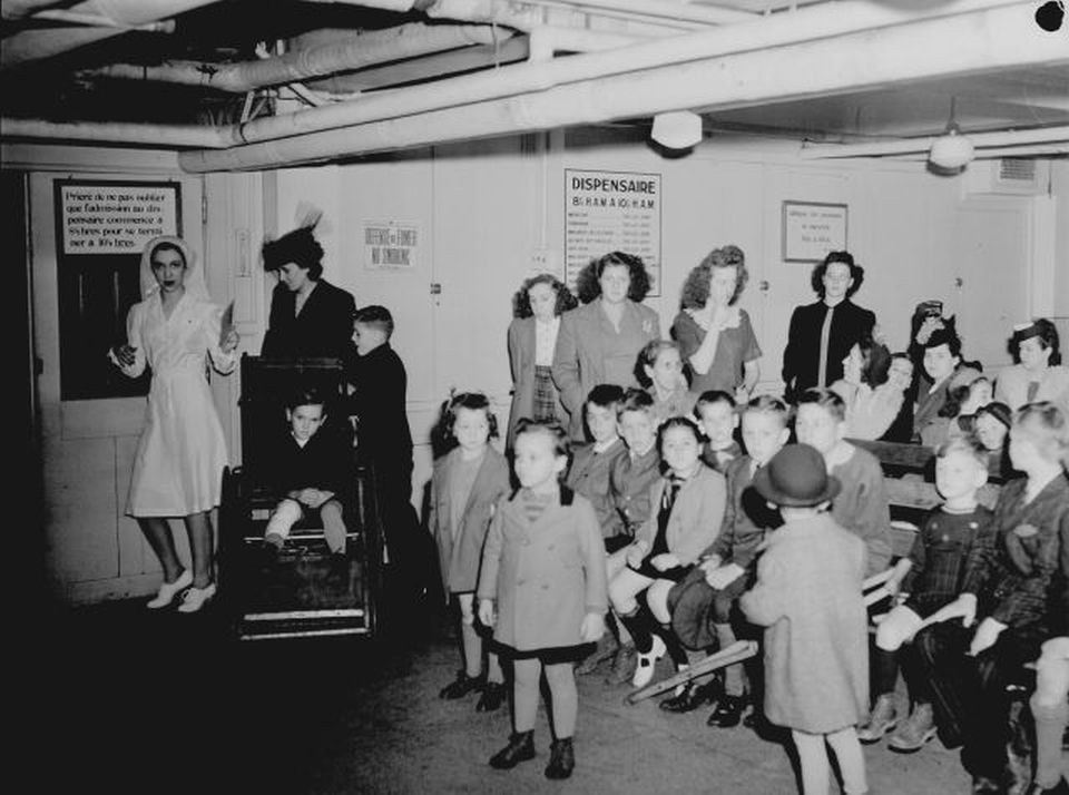 Clinic waiting room with children and caregivers; nurse beside a child in a wheelchair.